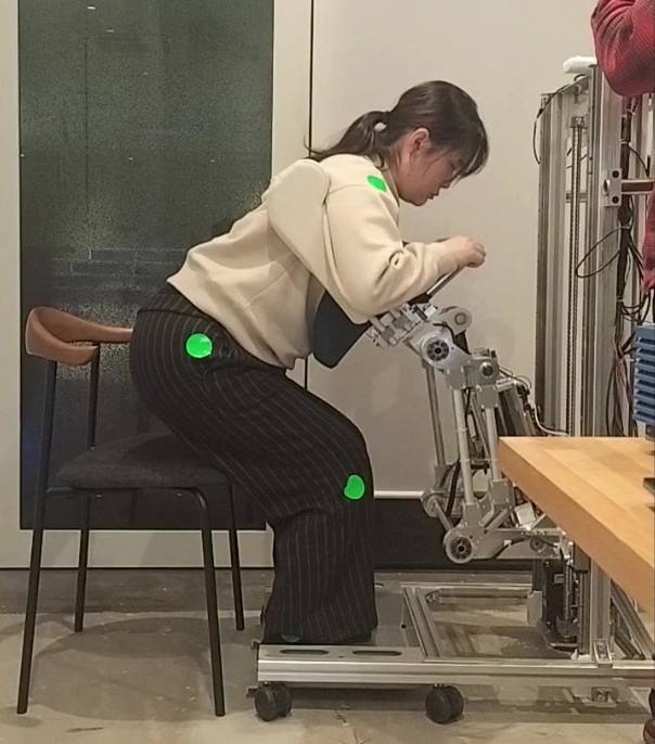 試作機のアームに支えられて、椅子から立ち上がろうとしている様子